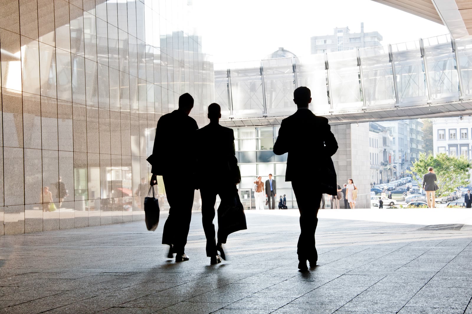 Three silhouettes walking out of a glass building
