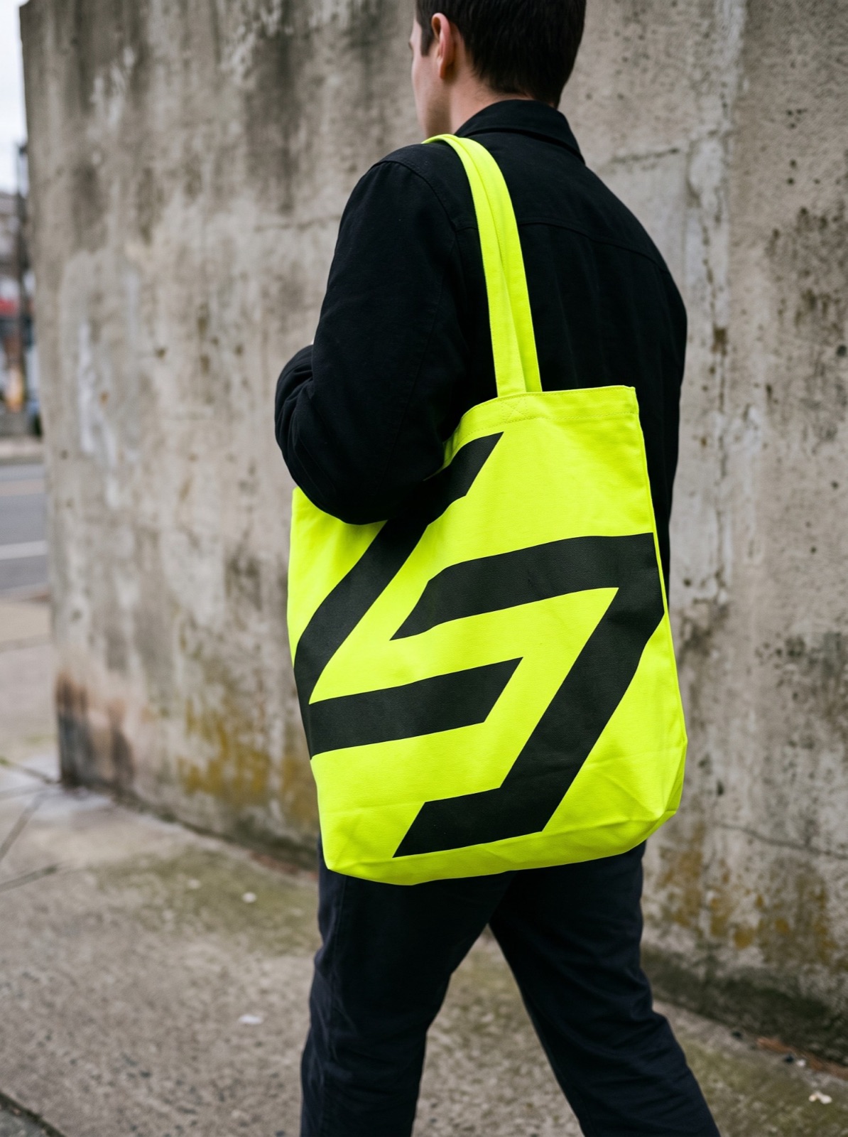 A lime tote bag with a giant black mark, carried down a street
